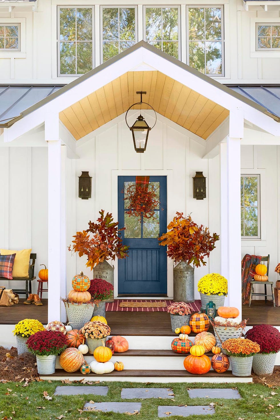 a front porch decorated for fall with loads of pumpkins, mums, fall leaves, bittersweet and metal buckets