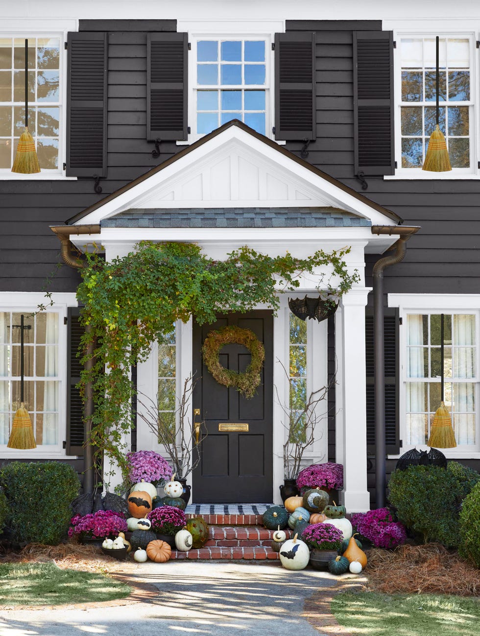 the front porch of a dark gray house decorated with bat, decorated pumpkins, and purple mums