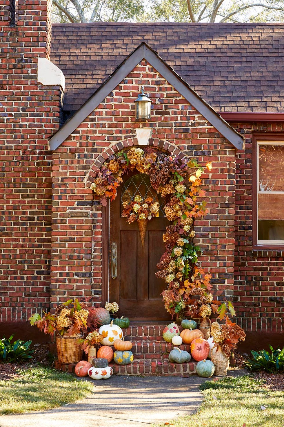 the door of a brkc house deocrated with fall leaves, dried hydrangea, and loads of pumpkins decorated with fall leaves