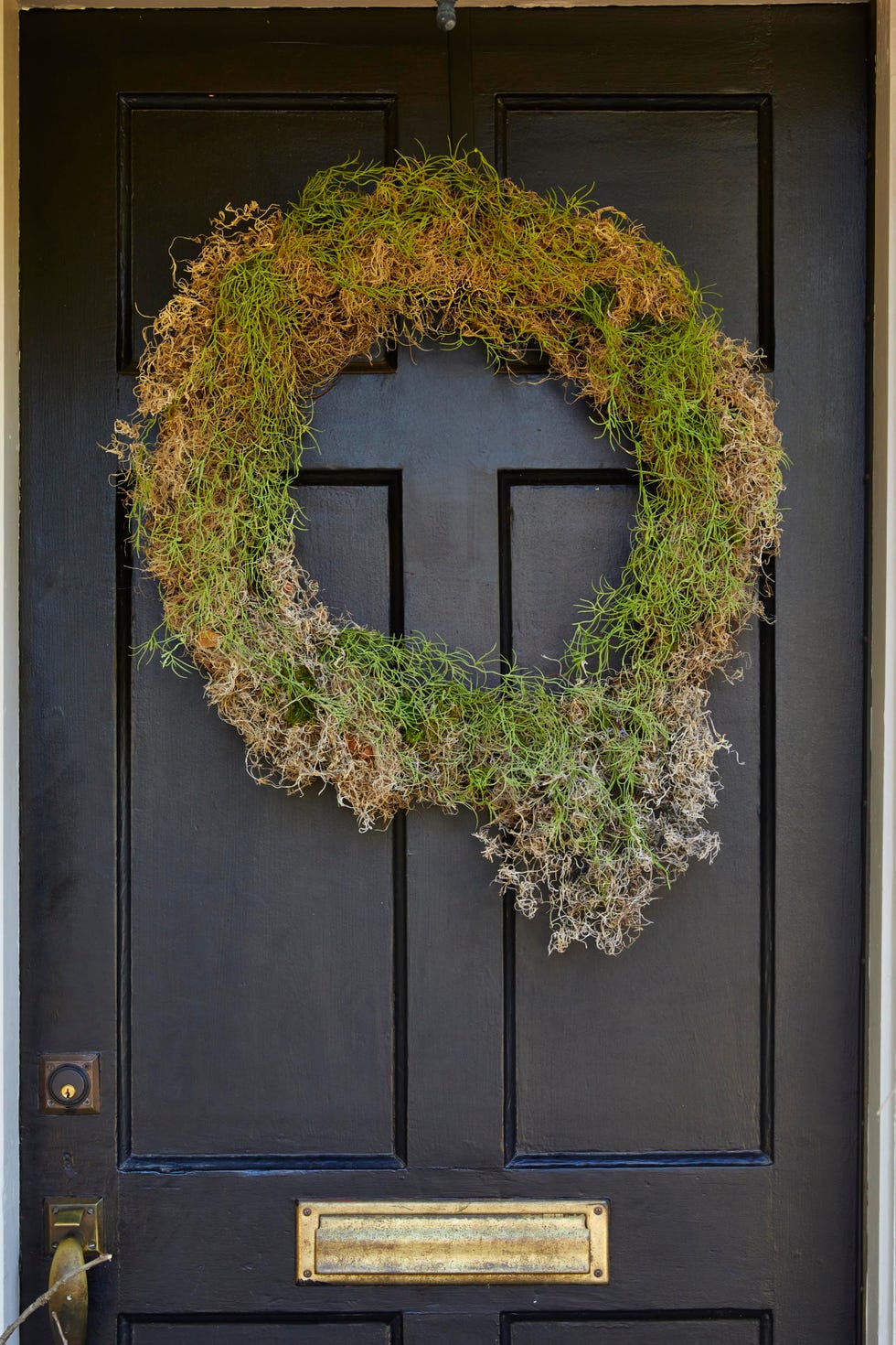 a wreath made from preserved moss hung on a black door