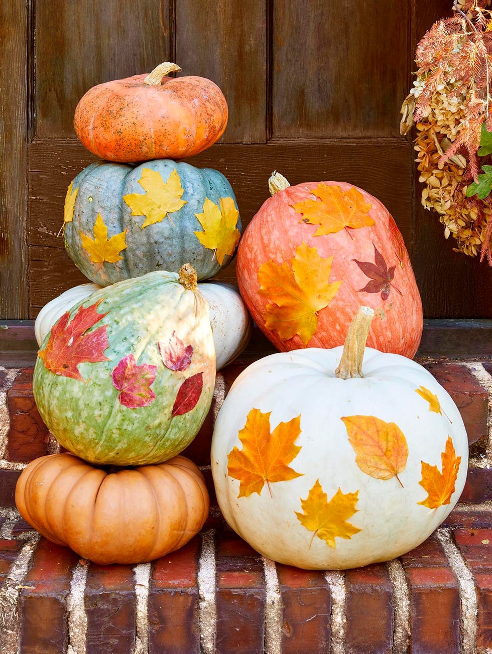 pumpkins decorated with colorful fall leaves set up brick stairs in fron of a wood door