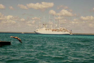 person diving into turquoise water with a large ship in the background