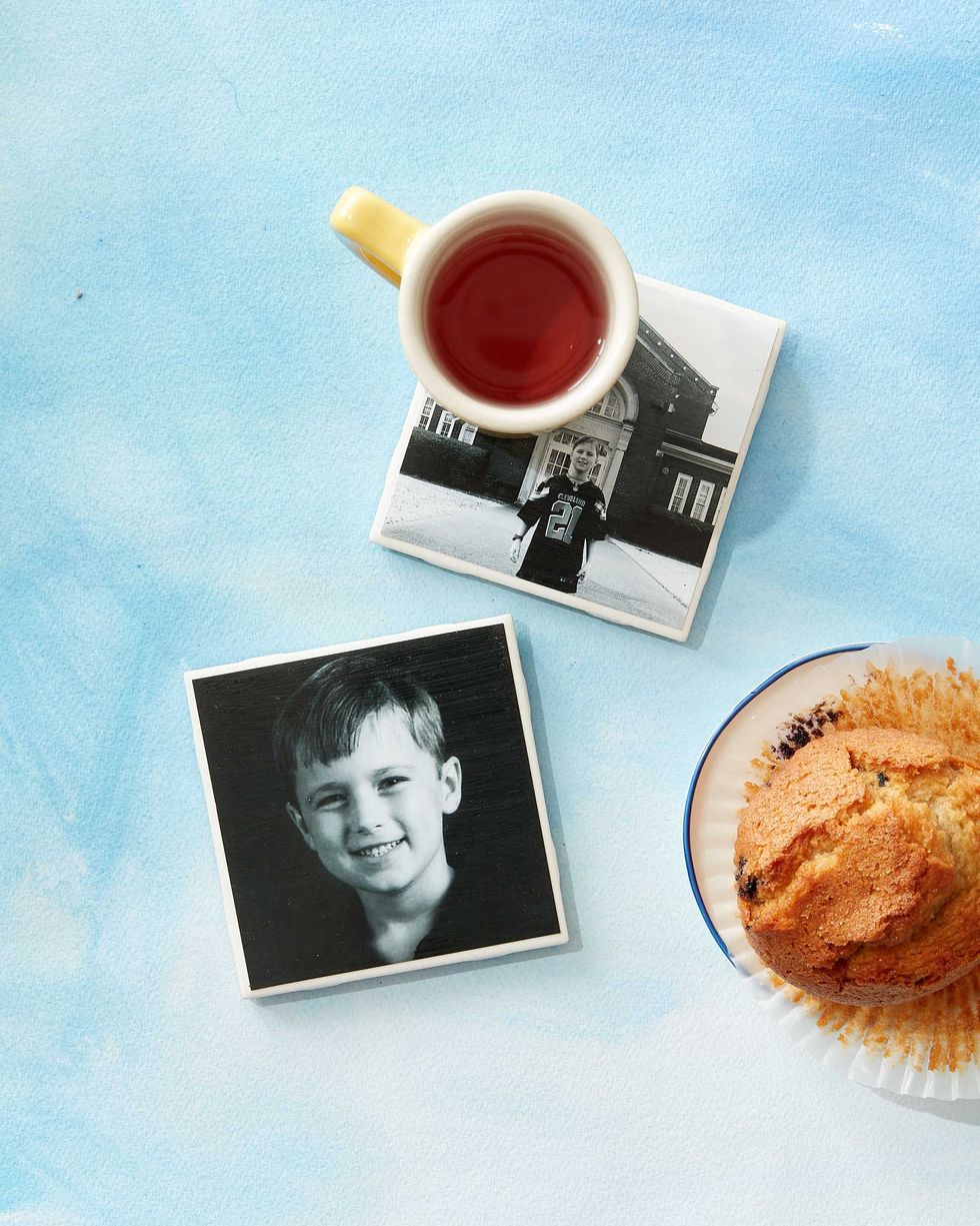 two square coasters decoupaged with black and white photos of a child, pictured with a cup of a hot tea and a blueberry muffin