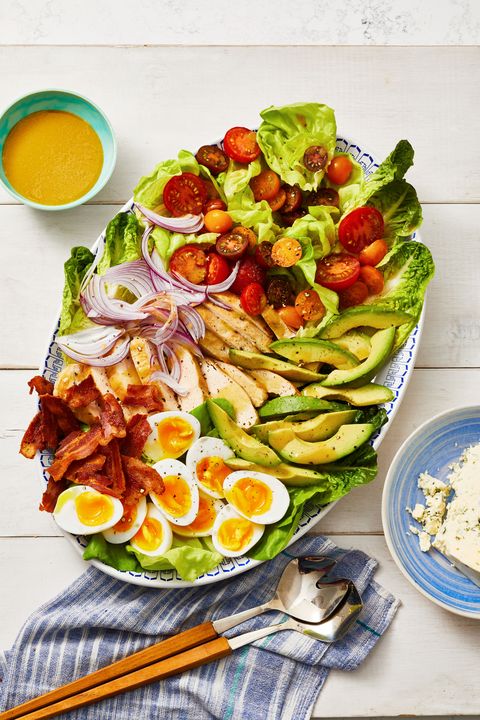 chicken cobb with avocados, tomatoes, red onions, bacon and soft boiled eggs on a plate