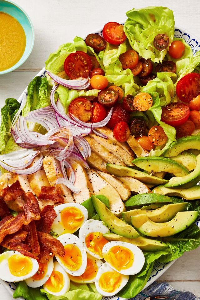 a cobb salad with avocados, red onions, soft boiled eggs, lettuce, and tomatoes