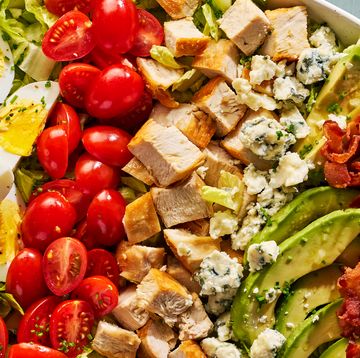 lettuce, bacon, avocado slices, hard boiled eggs, halves tomatoes, blue cheese and chicken pieces in a bowl