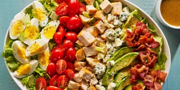 lettuce, bacon, avocado slices, hard boiled eggs, halves tomatoes, blue cheese and chicken pieces in a bowl