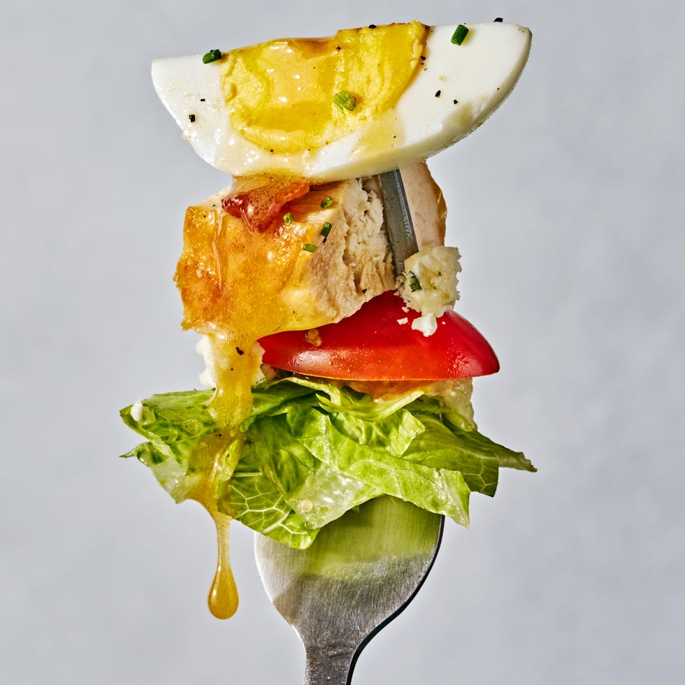 lettuce, bacon, avocado slices, hard boiled eggs, halves tomatoes, blue cheese and chicken pieces in a bowl