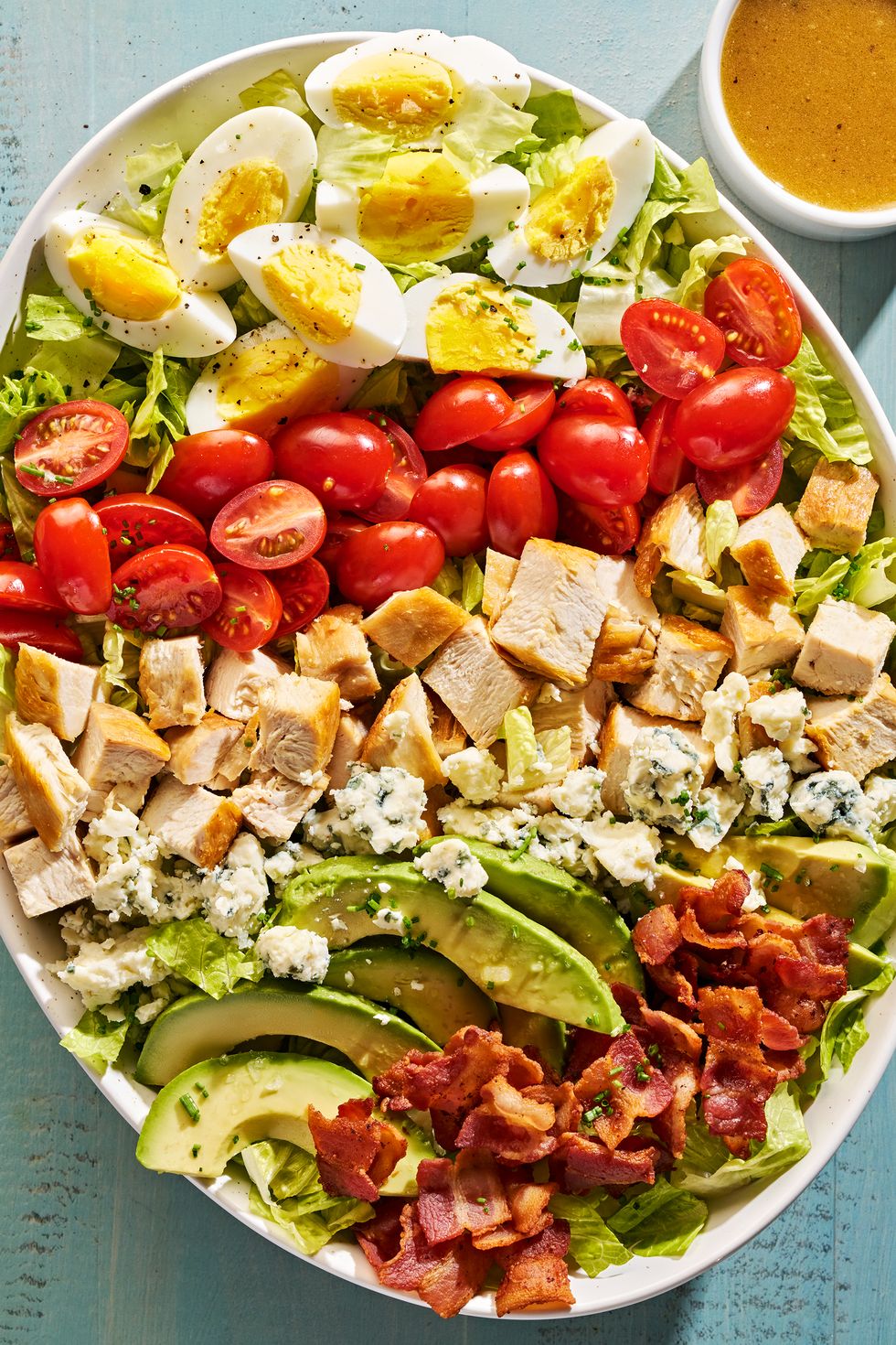 lettuce, bacon, avocado slices, hard boiled eggs, halves tomatoes, blue cheese and chicken pieces in a bowl