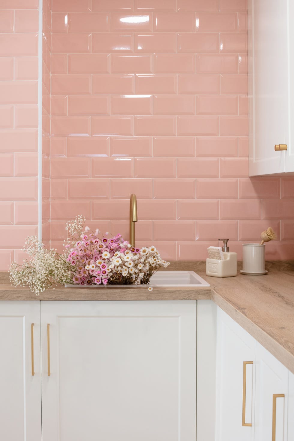 cocina con armarios blancos, fregadero con grifo dorado y frente de azulejos rosas