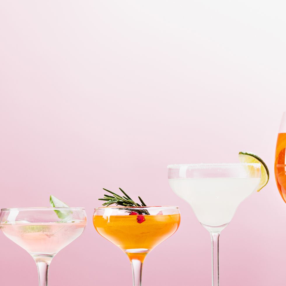three cocktails with fruit garnishes on table, against pink