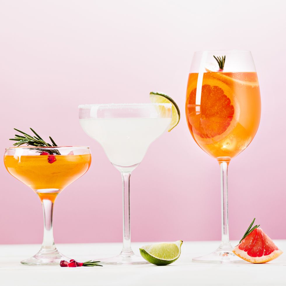 three cocktails with fruit garnishes on table, against pink