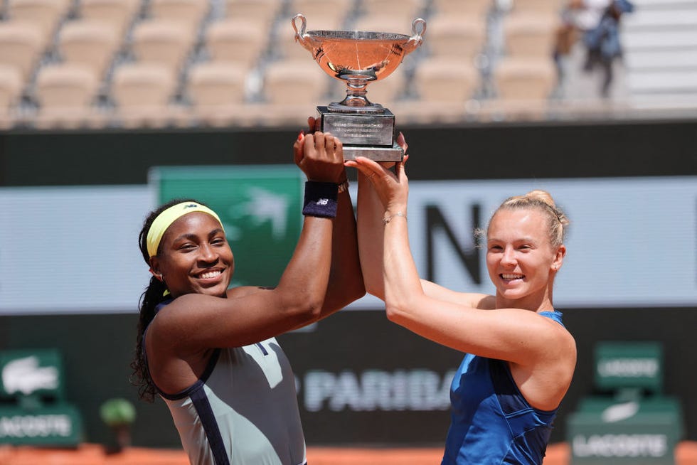 coco gauff and tennis partner katerina siniakova standing on opposite sides and holding up a trophy together