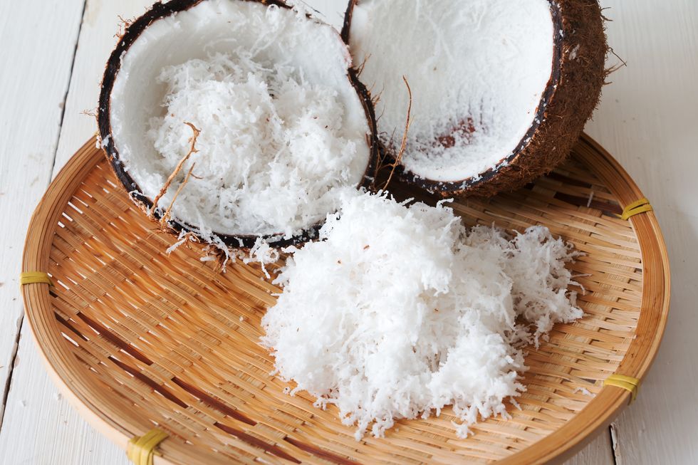 close up shot of fresh grated coconut flesh and coconut shell on bamboo tray