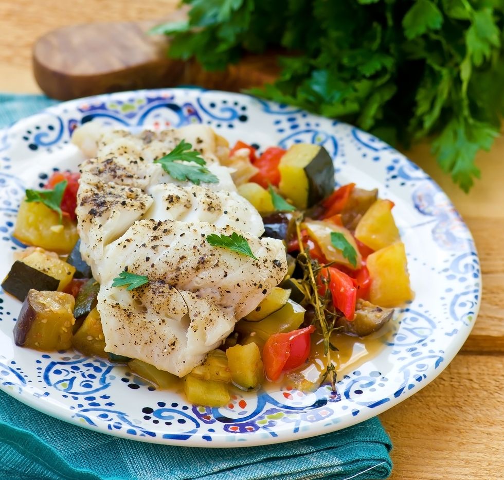 cod on a plate of vegetables, served on a white and blue patterned plate on a wooden surface.