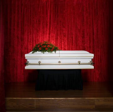 what is death? coffin on stage with red flowers on top and dramatic red curtains in the background