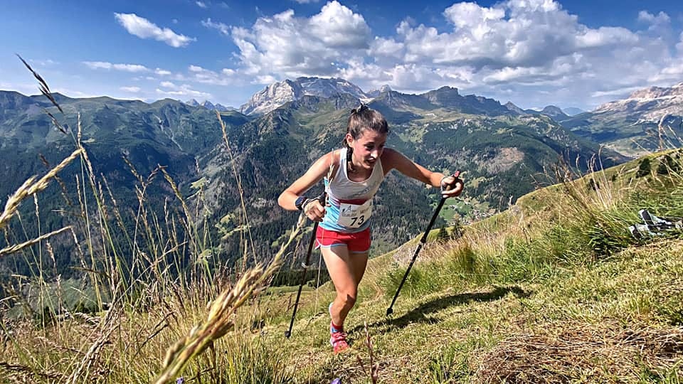 runner navigating a mountain trail with trekking poles against a scenic backdrop
