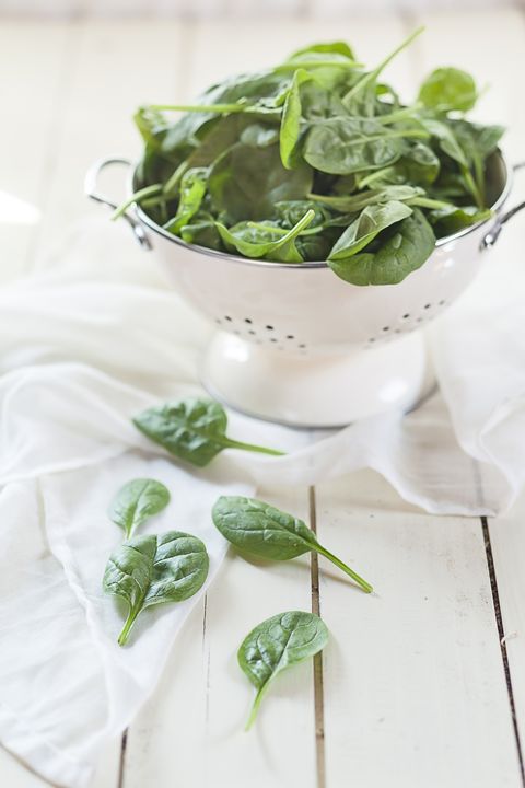 colander of fresh spinach leaves on white cloth and wood