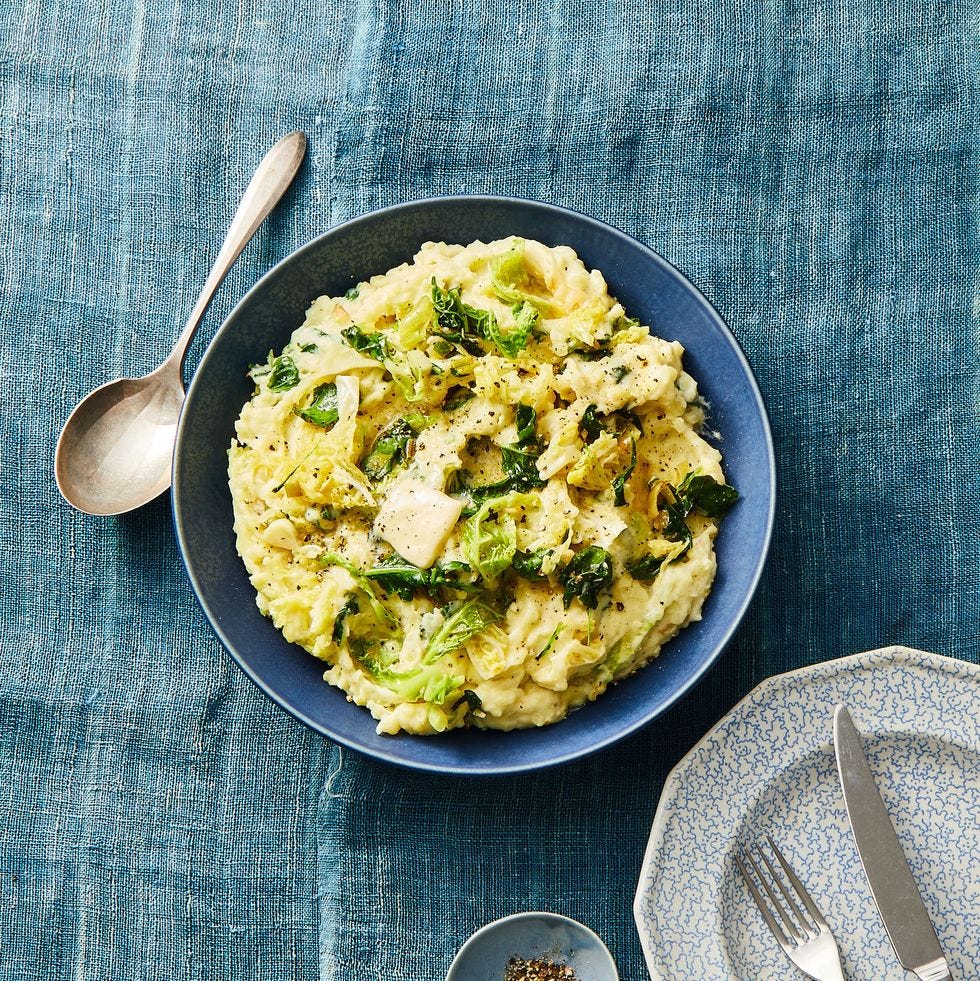 a blue bowl of beige colcannon with cabbage on top