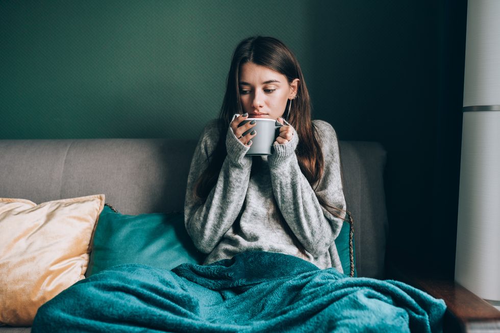 cold sick season, trying to get some warm sick young woman drink hot tea, wrapped in blanket in cold apartment