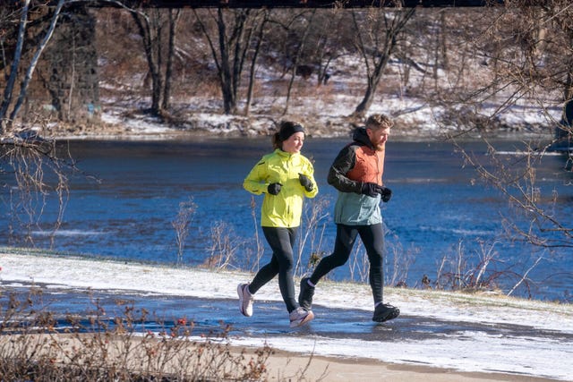 two individuals jogging along a snowy riverside path