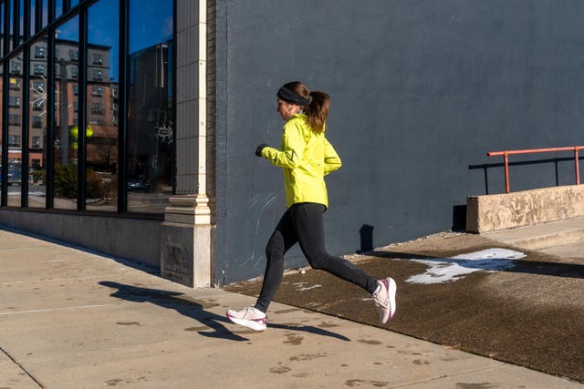 runner in bright yellow jacket jogging past a building with large windows