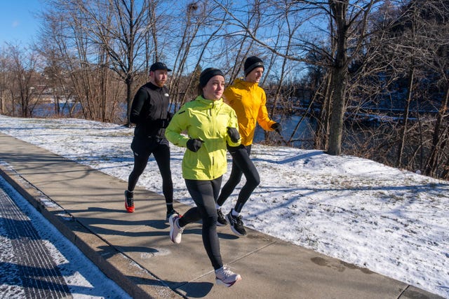 group of runners jogging on a snowy path beside a river