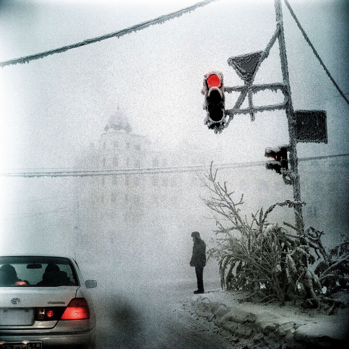 Een eenzame figuur staat op een straathoek in het Siberische Jakoetsk In de diepe vrieskou kon Fotograaf Steeve Iuncker telkens maar een kwartier achtereen fotos maken voordat zijn camera bevroor en het filmrolletje verbrokkelde