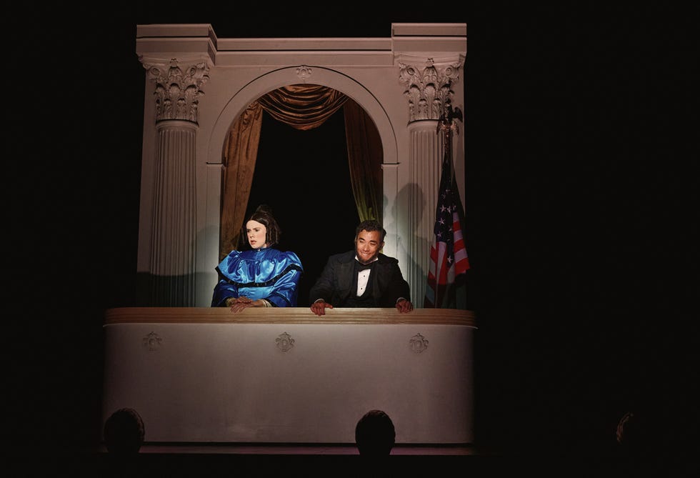 een theaterloge met twee formeel geklede personen die vanuit het publiek worden bekeken