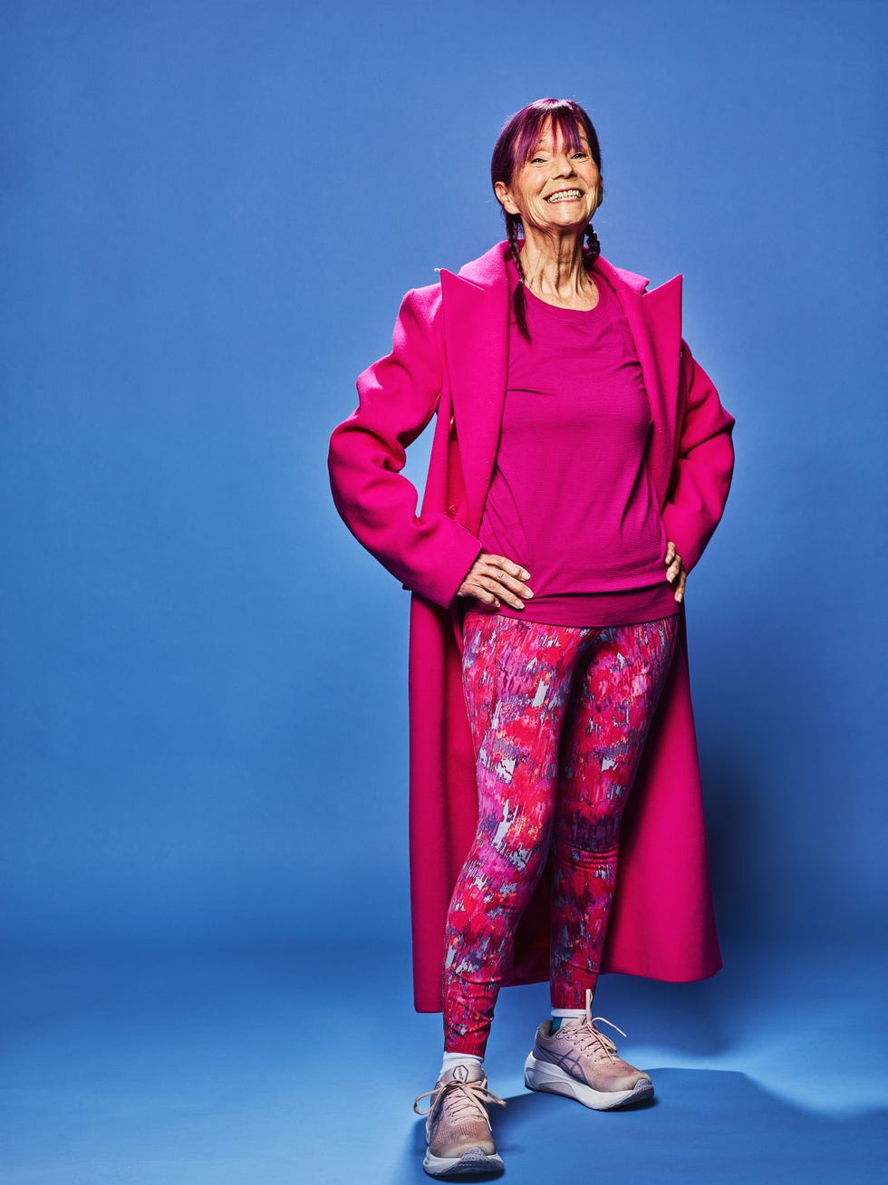 a person stands confidently with hands on hips wearing a vibrant pink coat matching top and patterned leggings