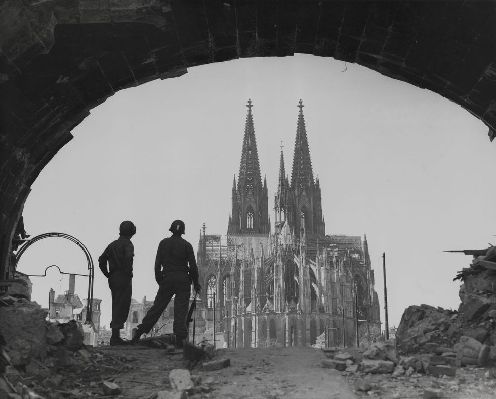 Van onder een van de bogen van de opgeblazen Hohenzollernbrcke bekijken twee Amerikaanse soldaten op 16 april 1945 de Dom van Keulen