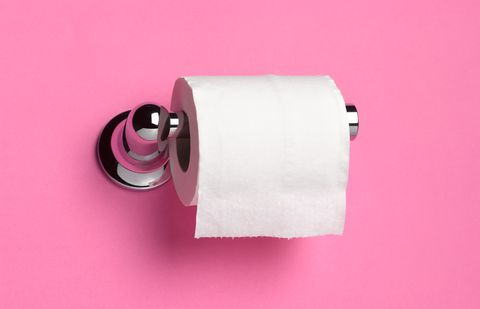 Roll of toilet paper on dispenser in front of pink bathroom wall.