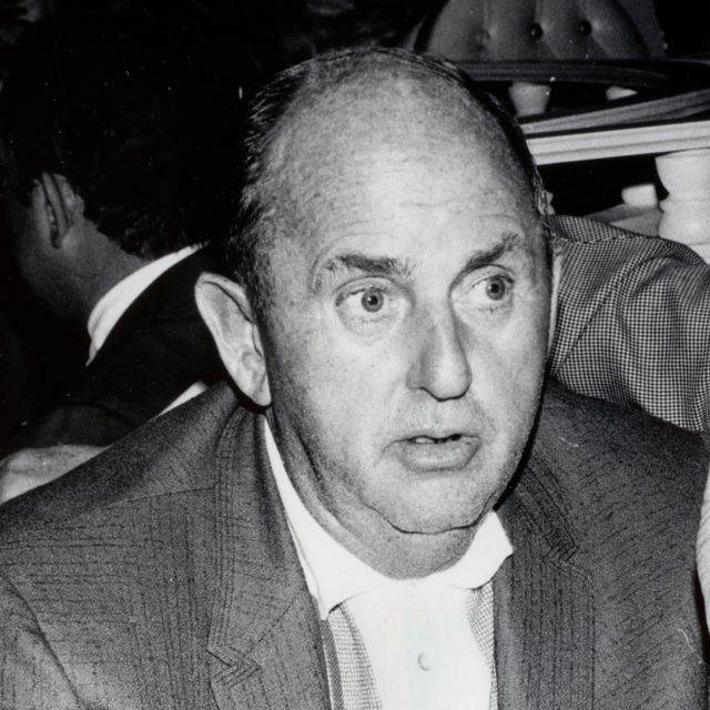 tom parker looks to the right of the camera in this black and white photo, his mouth is slightly open and he appears to be listening to someone else, he wears a suit jacket with a collared button up shirt