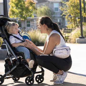 colugo lightweight stroller, a mom bends down to check her son in a black stroller, part of a good housekeeping review of colugo strollers