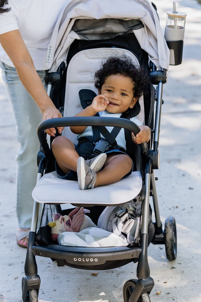 a baby with curly hair sits in a gray version of the colugo one stroller, part of a good housekeeping review of colugo strollers