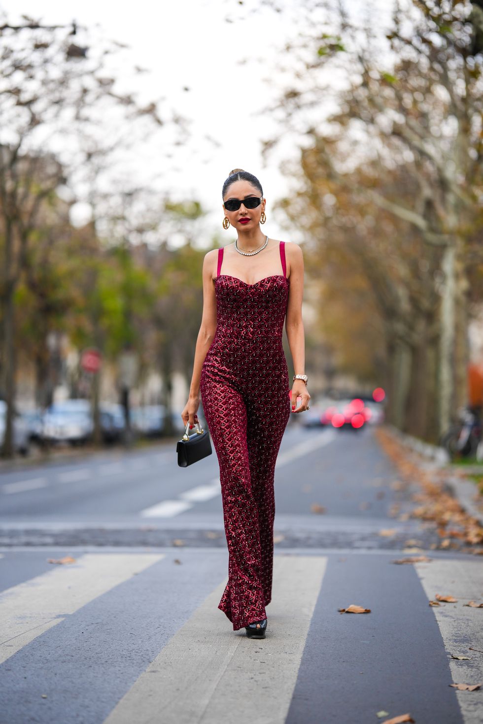 paris, france   november 14 patricia gloria contreras wears black sunglasses, gold earrings from louis vuitton, a gold chain necklace, a silver and rhinestones necklace, a burgundy velvet with red checkered embroidered sequins pattern  v neck  tank top  flared jumpsuit, a pink gold watch from rolex, a large gold ring, a black shiny leather handbag from alzuarr, black shiny leather pumps heels shoes with small open toe cap, during a street style fashion photo session, on november 14, 2021 in paris, france photo by edward berthelotgetty images