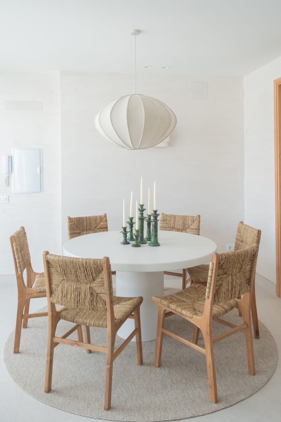 mesa de comedor blanca redonda con sillas de fibras y lámpara suspendida