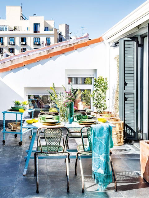 un comedor en la terraza con mesa azul y sillas verdes de metal perforado