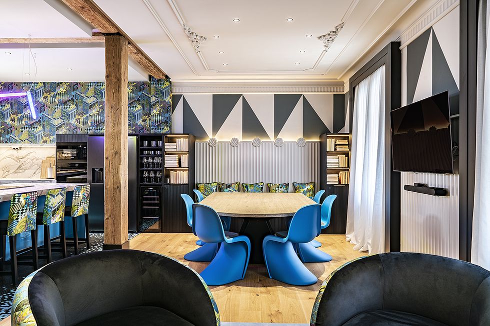 comedor con mesa de madera, sillas panton de plastico azules y paredes decoradas con molduras y dibujos geomtericos en blanco y negro