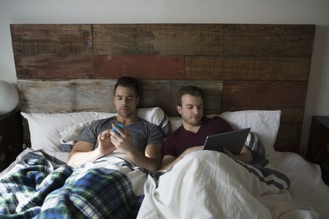 Comfortable homosexual couple using digital tablet and cell phone in bed