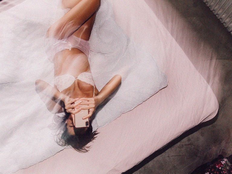 a person lying on a bed in lingerie on their phone