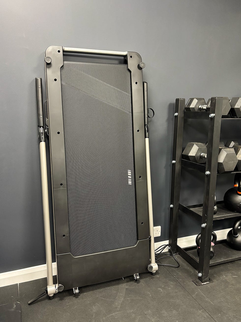 folded treadmill positioned against a wall beside a weight rack
