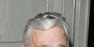 stephen sondheim smiles at the camera, he wears a brown quarter zip jacket over a dark colored tshirt