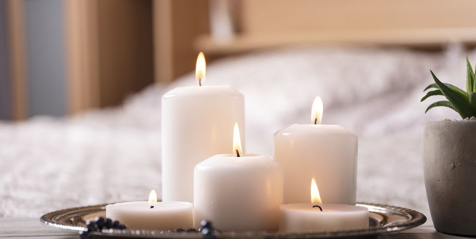 composition of white burning candles on bedside table in light cozy bedroom interior selective focus