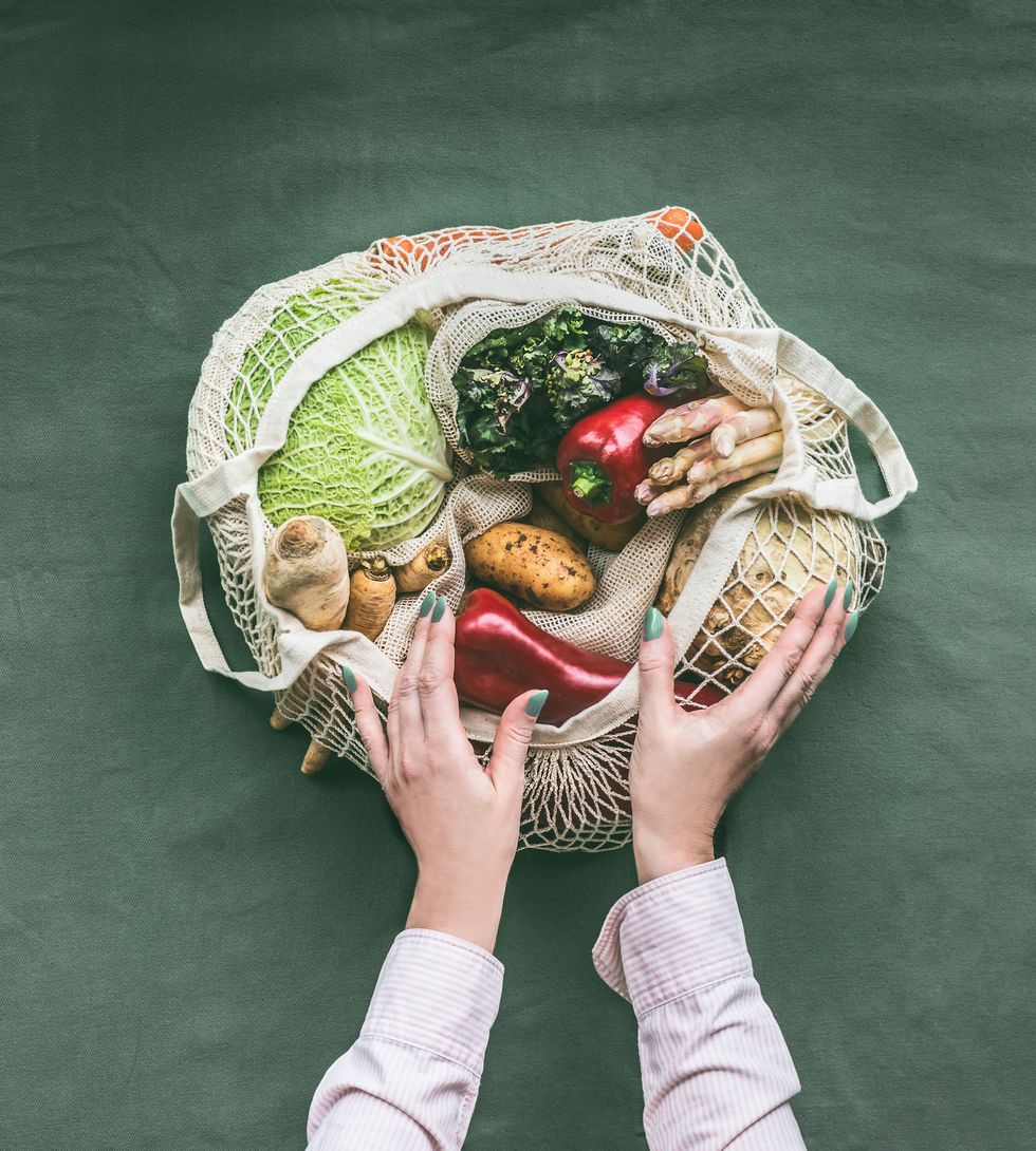 female hands holding eco friendly mesh grocery shopping bag with various vegetables on dark background , top view plastic free and zero waste lifestyle concept