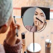 woman applying concealer with brush with magnifying mirror
