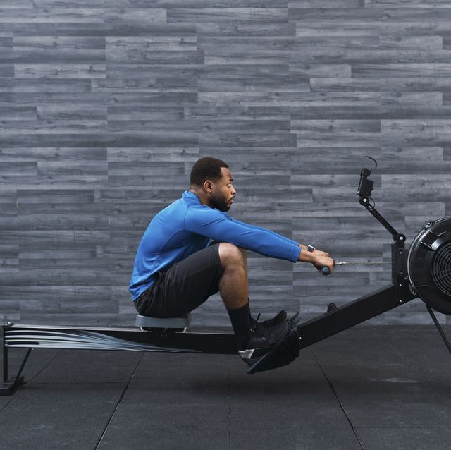 concentrated athlete exercising on rowing machine in front of wall in gym