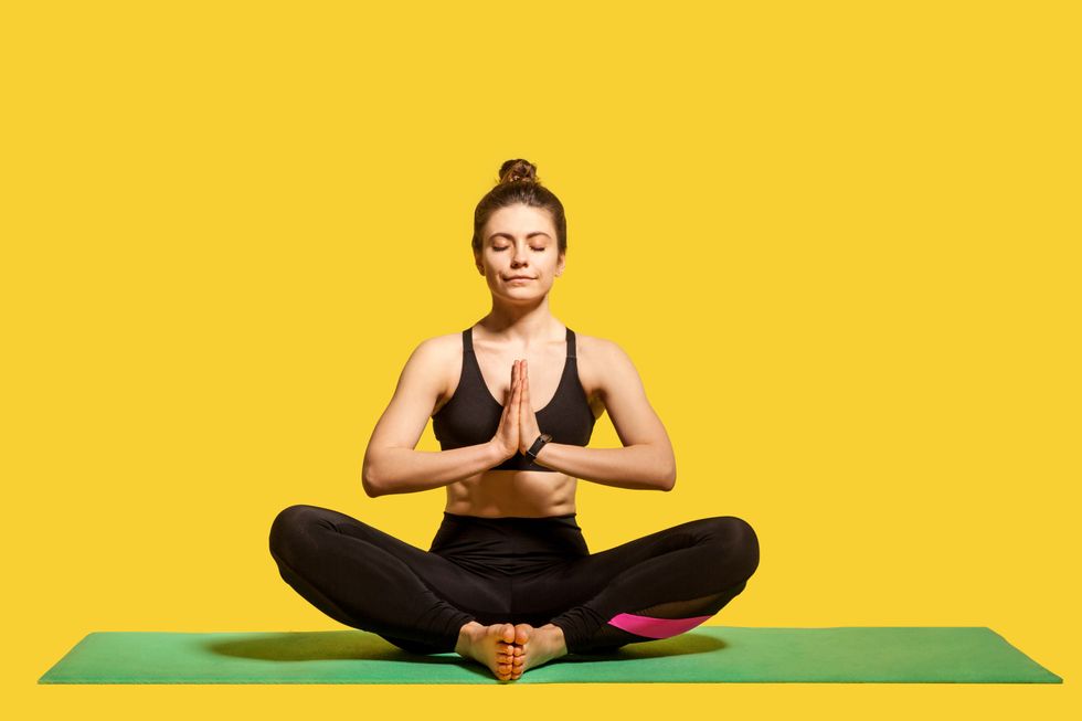 concentrated peaceful woman with hair bun in tight sportswear sitting on mat practicing yoga, holding hands in namaste
