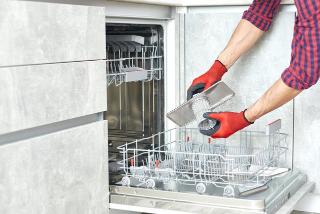 concept maintenance service of home appliances worker cleans filter in the dishwasher male repairman checking food residue filters