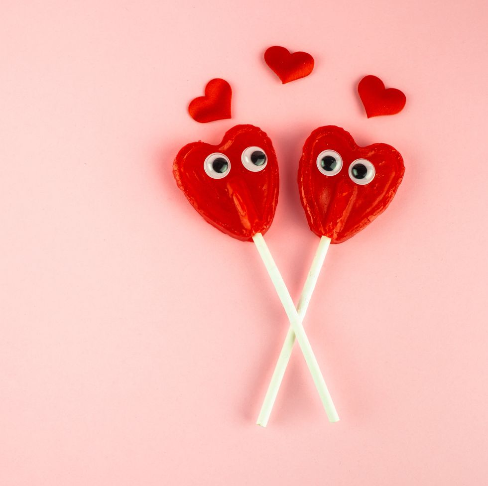 Concept of love and romanticism. Two red heart lollipops with eyes looking at each other and several red hearts